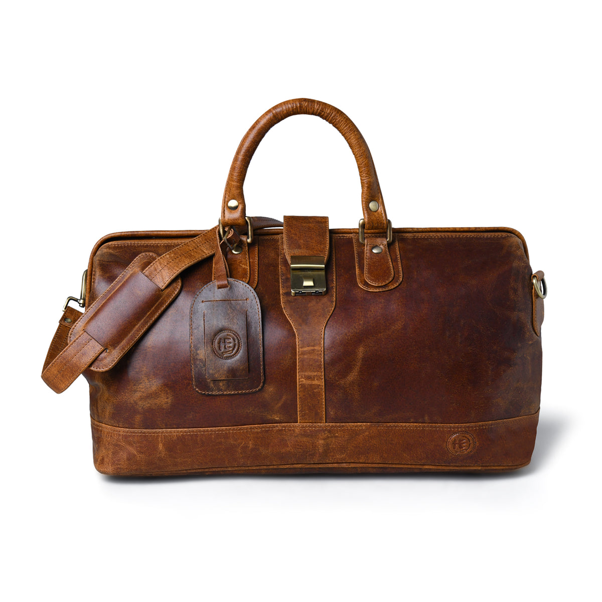 tan brown leather duffel bag with dual top handles, a detachable shoulder strap, a front leather luggage tag, and brass-tone hardware, photographed on a clean white background.