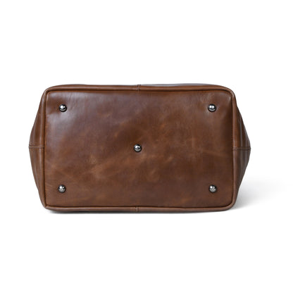 The bottom view of a Espresso brown leather tote bag, showing its distressed finish and four silver metal studs on a white background.