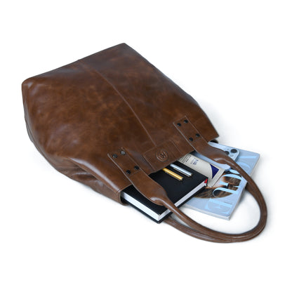 A Espresso brown leather tote bag shown at an angle on a white background, with books and a tablet partially tucked inside to demonstrate its capacity.