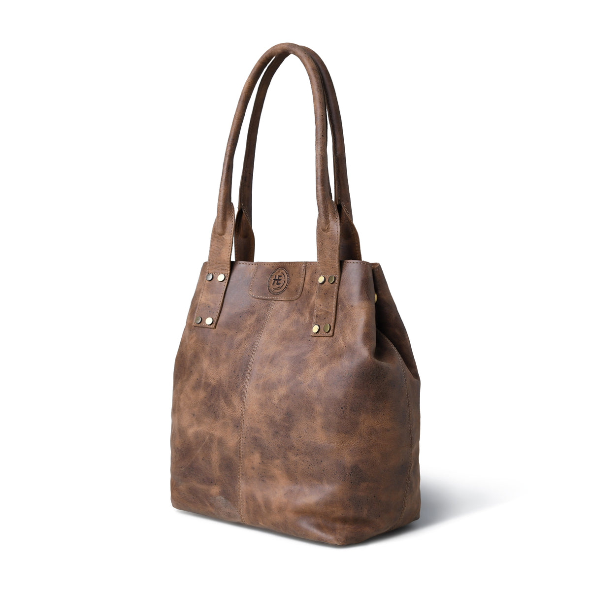 A Tan brown distressed leather tote bag with double shoulder straps, gold-tone hardware, and a circular embossed logo on the front, shown against a plain white background.
