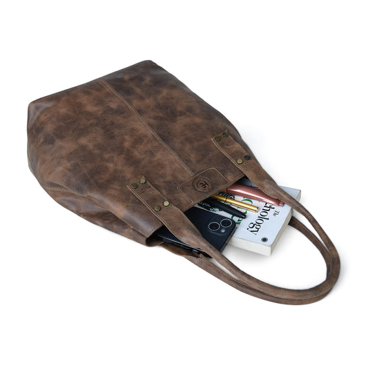 A Tan brown distressed leather tote bag with long handles, shown open with a smartphone, magazine, and notebook partially visible inside, on a clean white background.