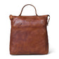 A brown leather tote bag with a top handle, front slip pocket, and a small embossed brand patch, shown on a plain white background.