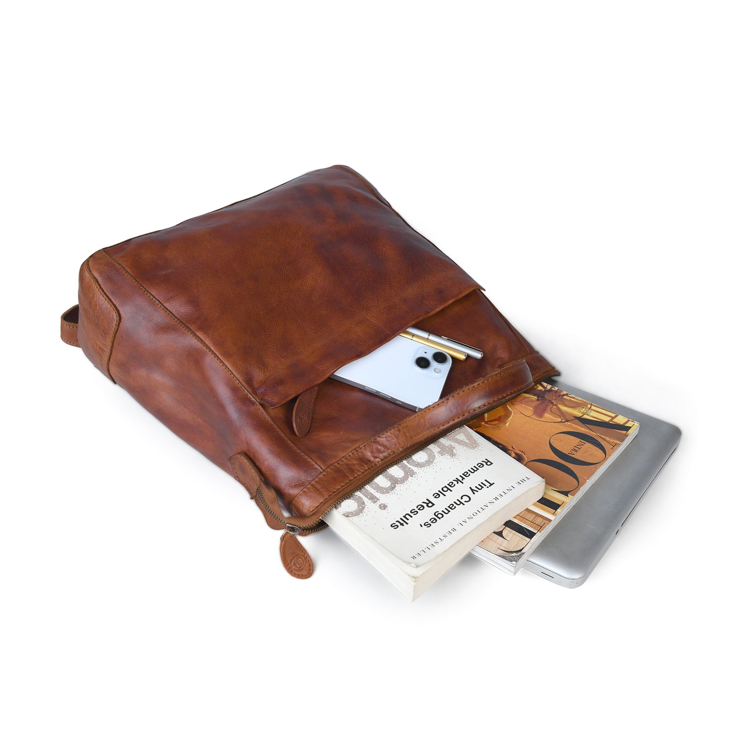 A brown leather backpack shown on a white background, with its front pocket open and containing a white smartphone, a book, and a silver laptop.