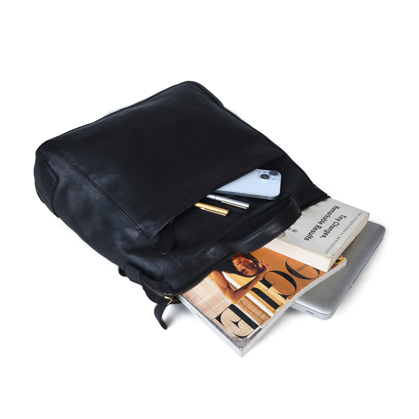 A black leather backpack shown open on a white background, with a smartphone, pens, a magazine, and a laptop partially visible inside.