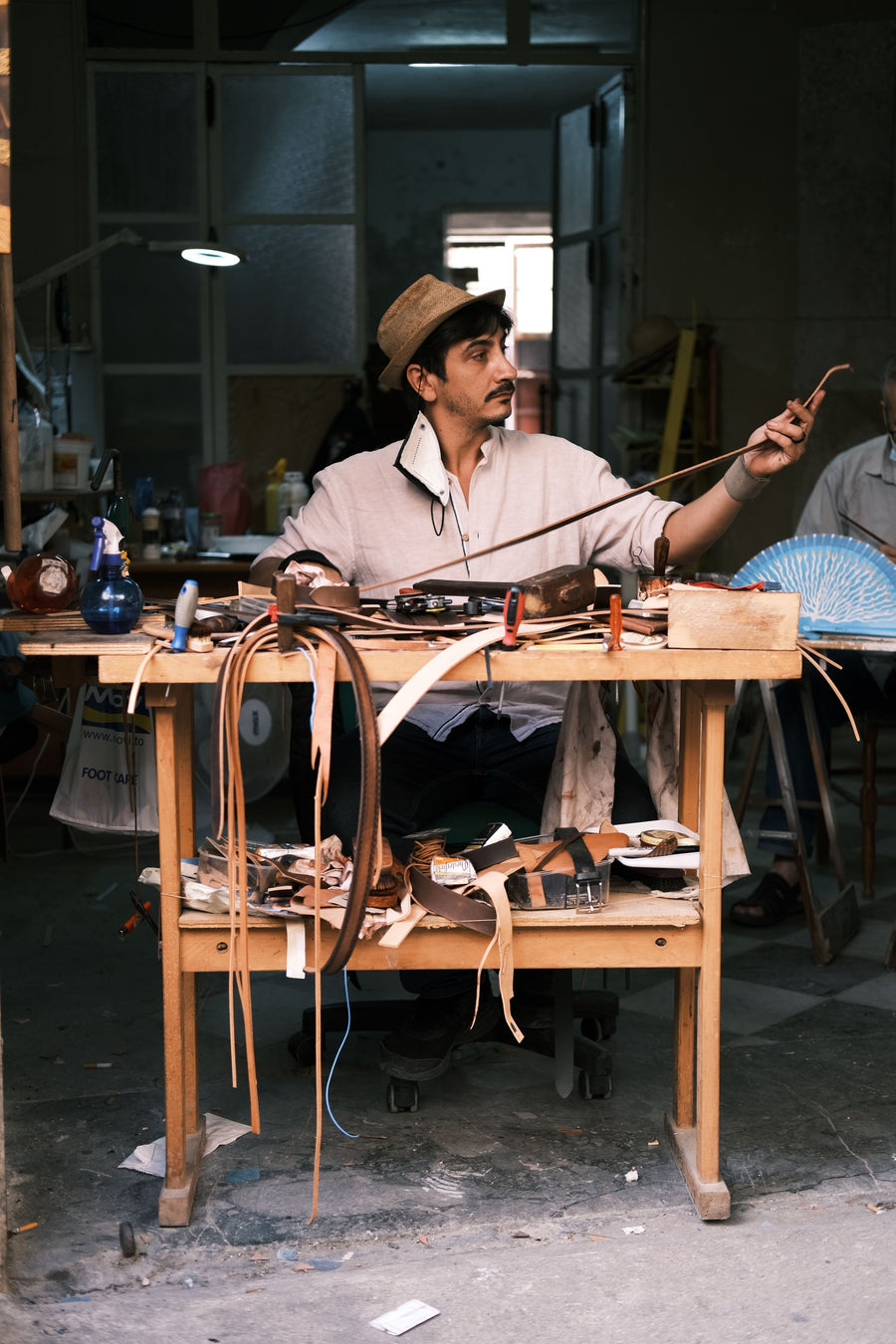 image of tailor sitting on a table doing his craftmanship on leather